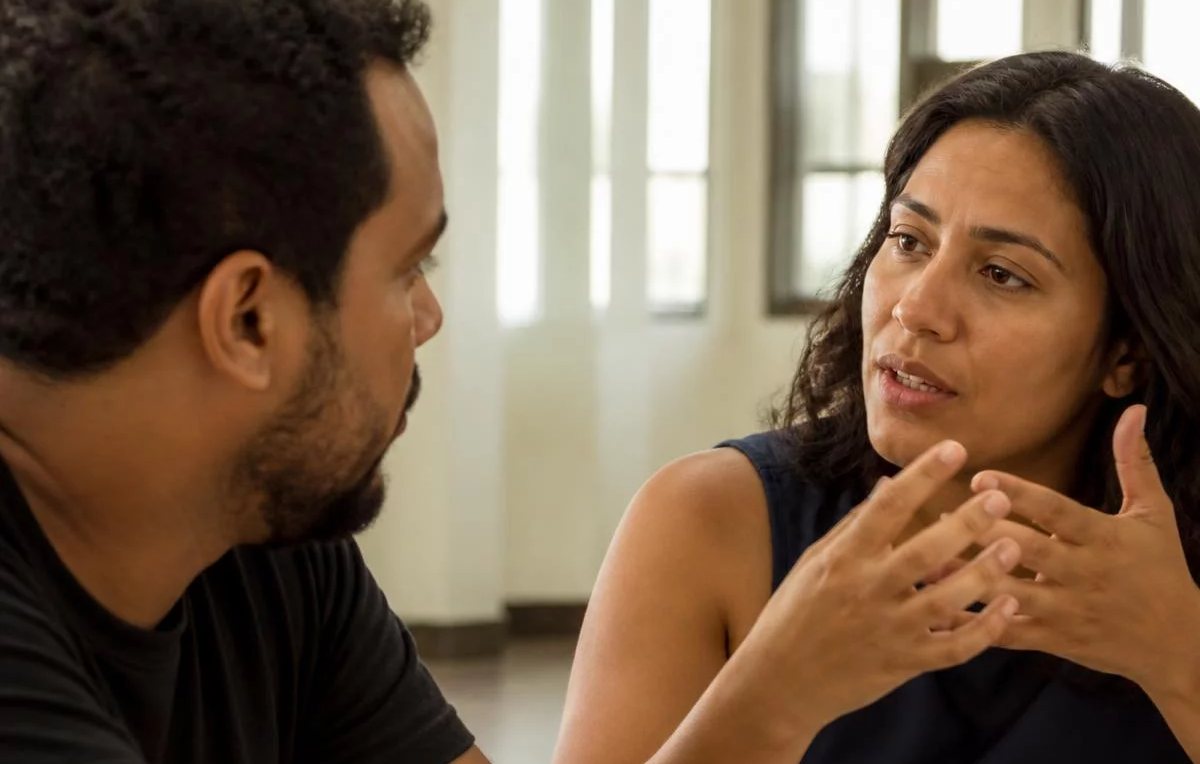 Duas pessoas sentadas de frente uma para a outra à mesa: uma fala, a outra registra por escrito